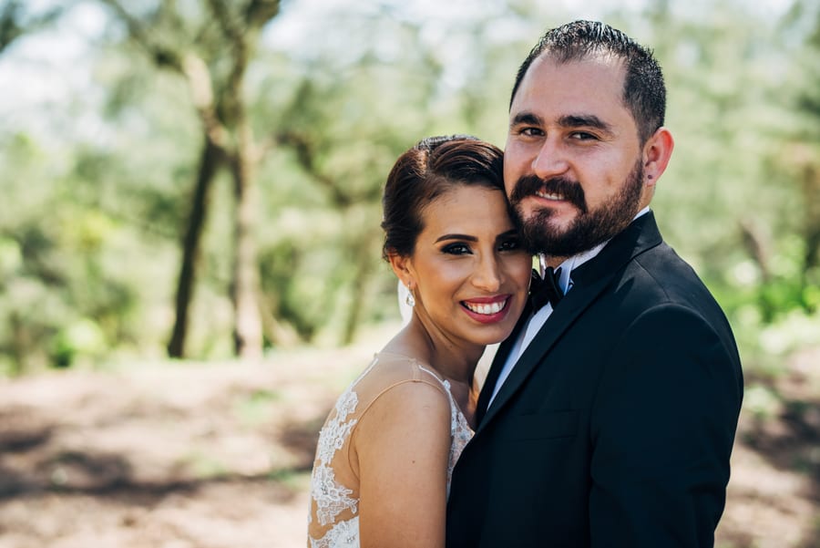Novios sonriendo mejilla con mejilla entre los árboles