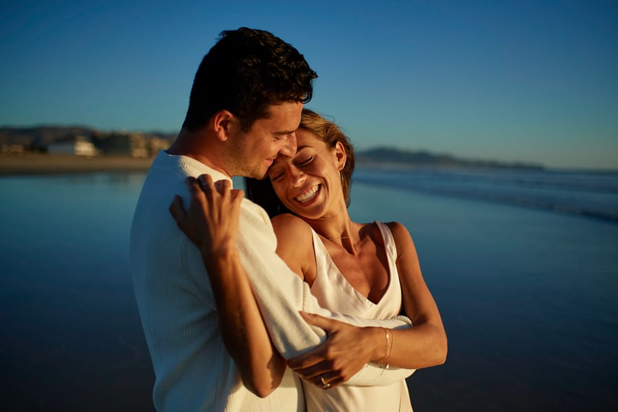 Pareja abrazada riendo en la playa al atardecer